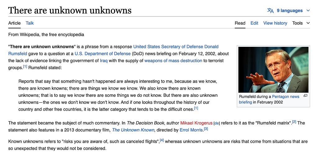 Wikipedia screenshot of the unknown unknowns article: the phrase in bold, the known-knowns quote, and a photo of Donald Rumsfeld in a suit and a dark navy tie with light dots